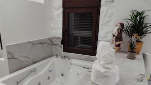A modern bathroom with a marble bathtub, a built-in heater, a window with blinds, and a small plant on the counter. - Lūma Retreat (Kastoria)