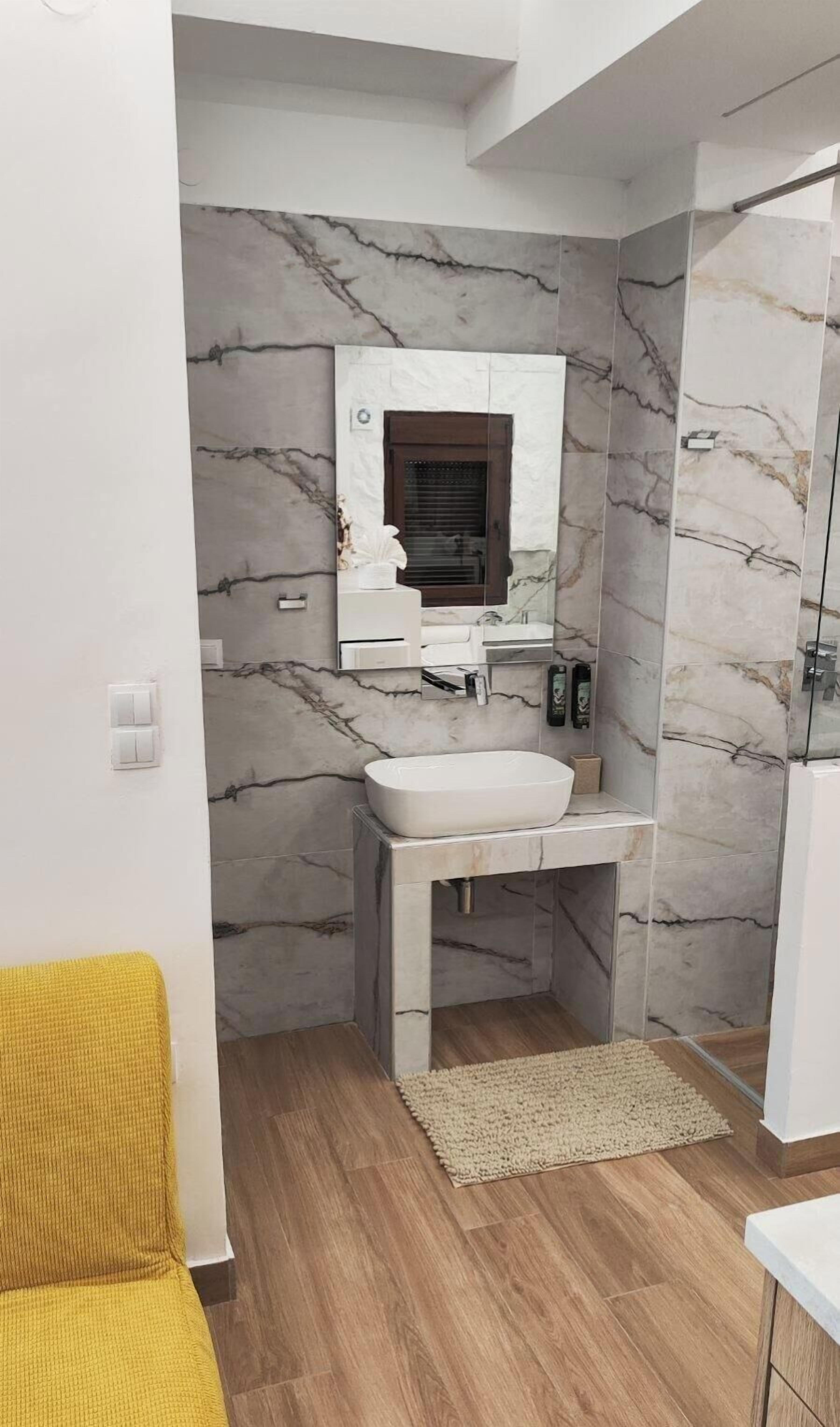 A bathroom with marble walls, a white sink, and a yellow chair.
