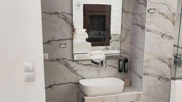 A bathroom with marble walls, a white sink, and a yellow chair.