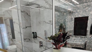 A modern bathroom with a glass shower enclosure, a marble-tiled wall, a sink, and a potted plant. - Lūma Retreat (Kastoria)