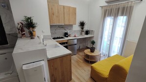 A compact kitchen with a built-in oven, a sink, and wooden cabinets. There is a small dining area with a round table and a yellow chair. - Lūma Retreat (Kastoria)