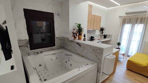 A modern living room with a large white bathtub, a yellow sofa, and a kitchen area with wooden cabinets and potted plants. - Lūma Retreat (Kastoria)