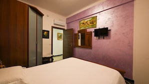 A hotel room with a bed, a wooden wardrobe, a wall-mounted TV, and a door leading to another room. - La Tana di Misha - Genova (Genova)