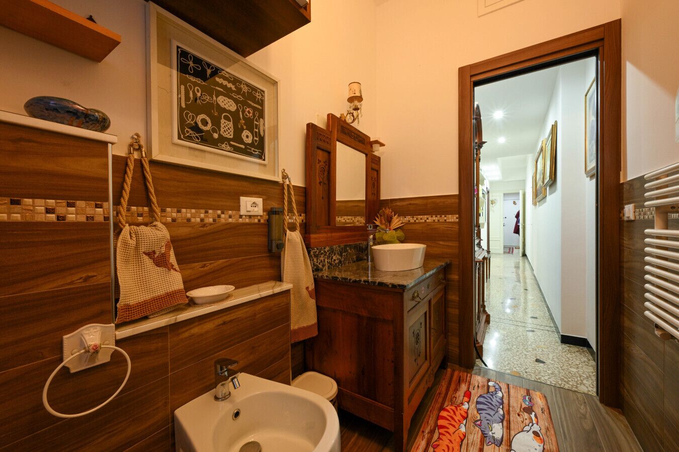 Un baño con tocador de madera, lavamanos y espejo. Hay un perchero con toallas y un cuenco decorativo en la encimera.