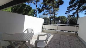 Een terras met een tafel en twee stoelen, een witte balustrade en bomen op de achtergrond.
