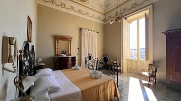 A hotel room with a large bed, a desk, a chair, a wardrobe, and a view of the city through the window.