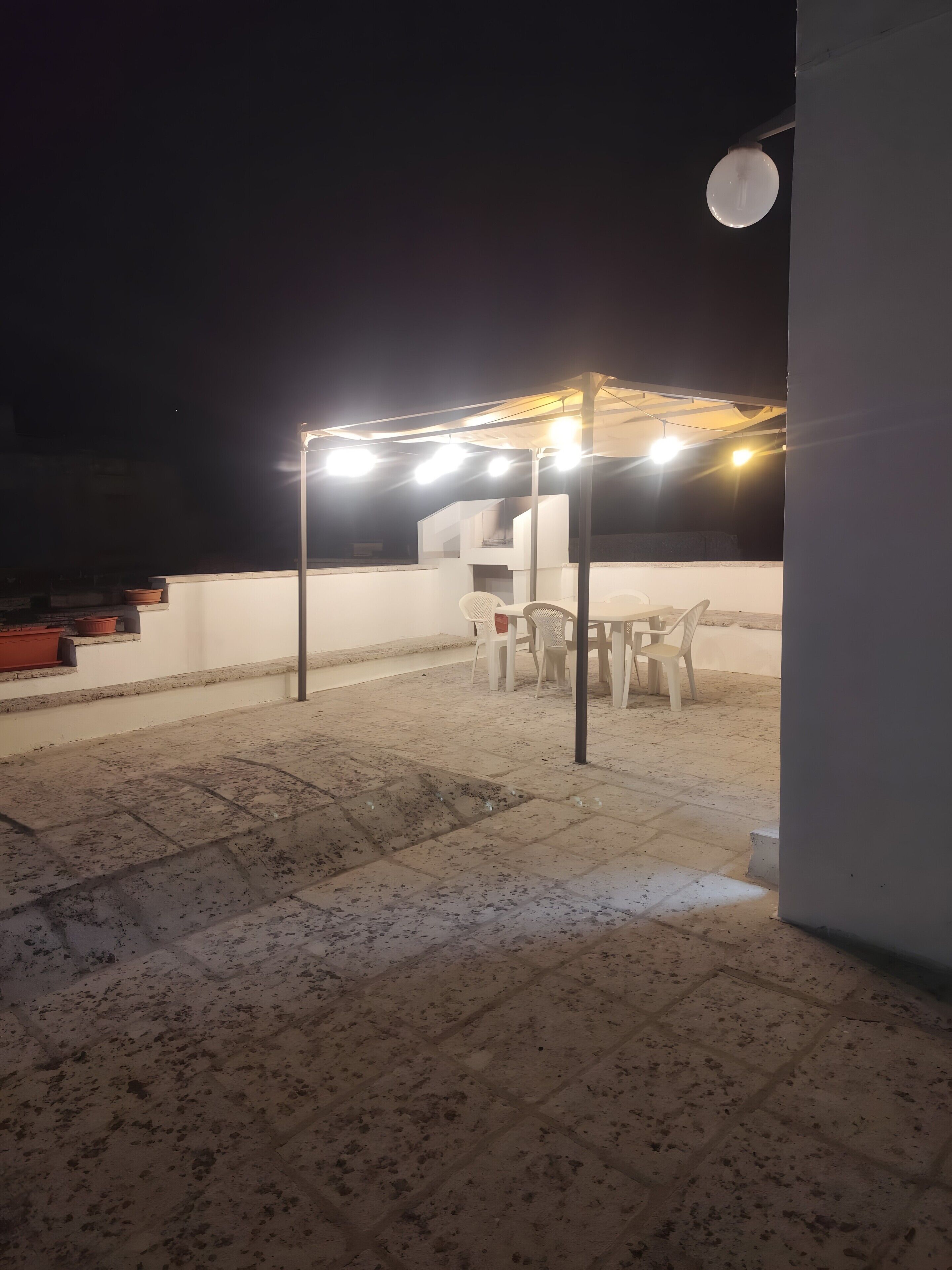 Une terrasse sur le toit avec une table et des chaises, une pergola illuminée et un escalier.
