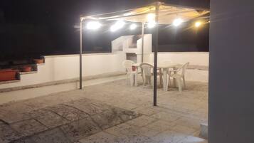 Une terrasse sur le toit avec une table et des chaises, une pergola illuminée et un escalier.