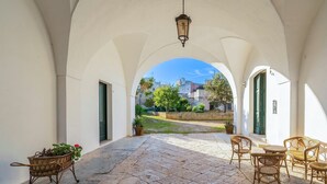 Eine Terrassensitzgelegenheit mit Blick auf Gebäude, ein Korbstuhl, ein Tisch und ein Blumentopf.
