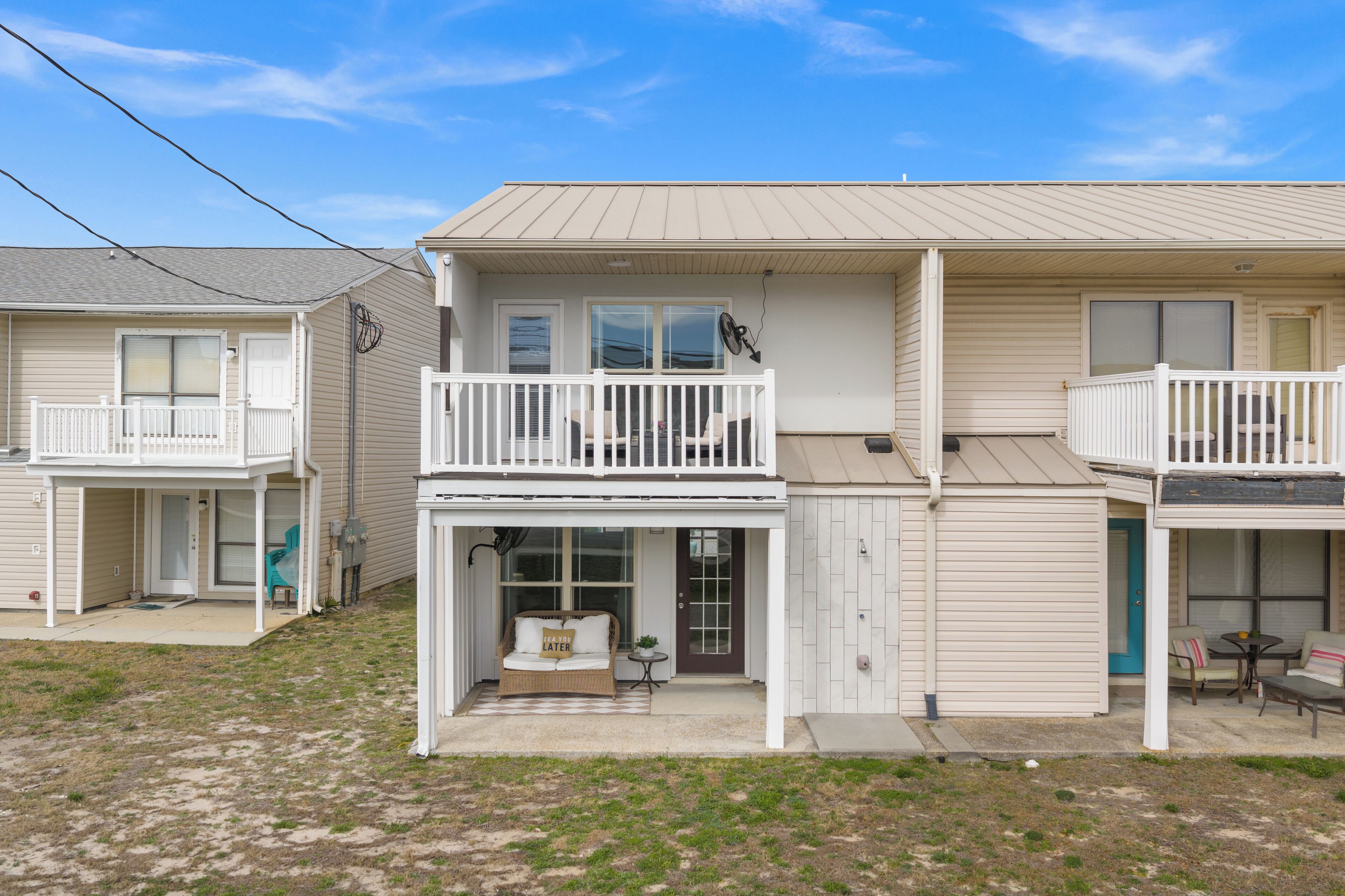 A two-story residential building with a balcony, a porch with seating, and a small outdoor table.