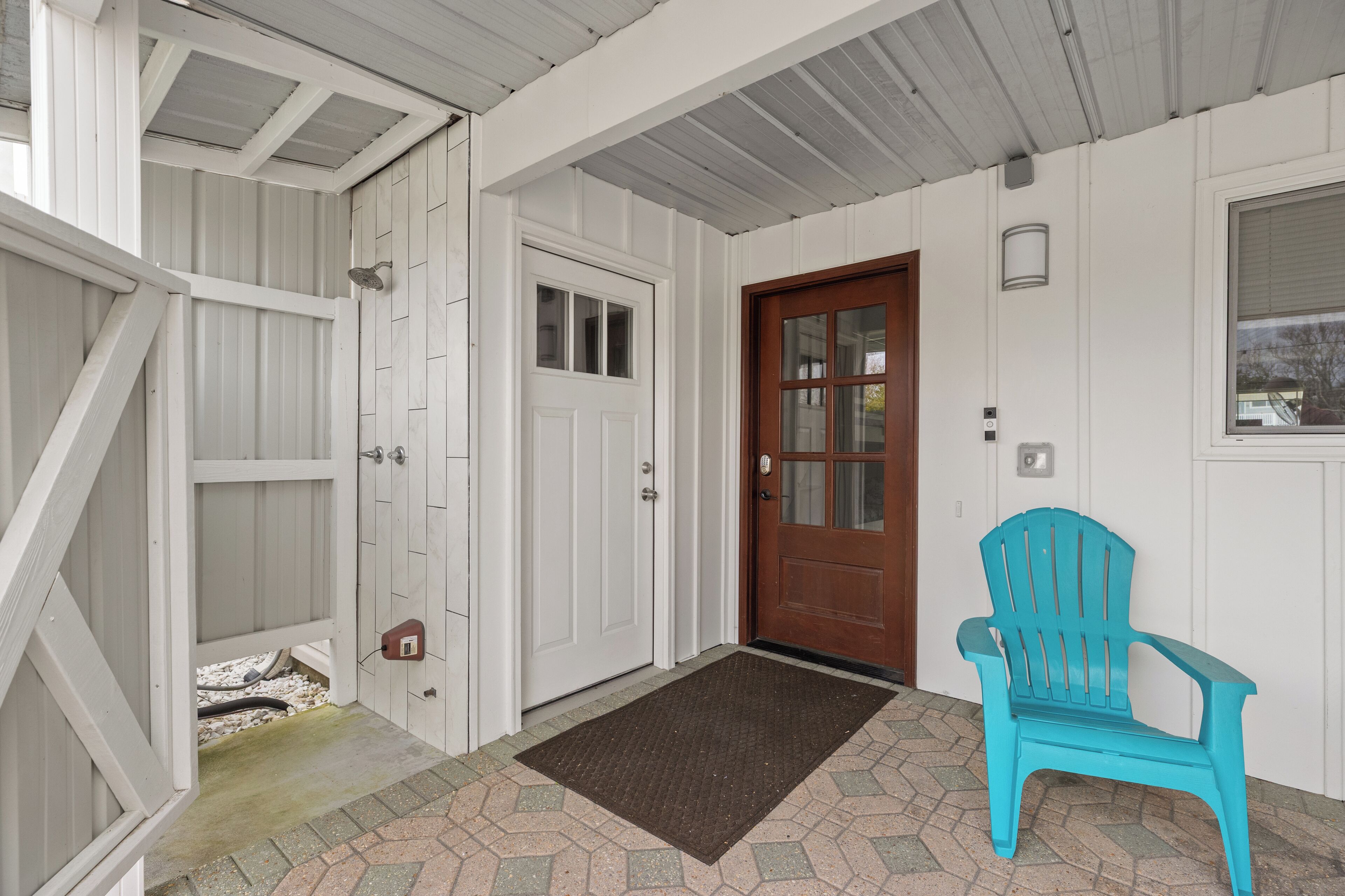 A porch with a wooden door, a blue chair, and a doormat.