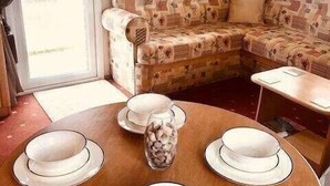 Una sala acogedora con un sofá y una mesa redonda preparada para comer, con platos blancos y un jarrón decorativo.