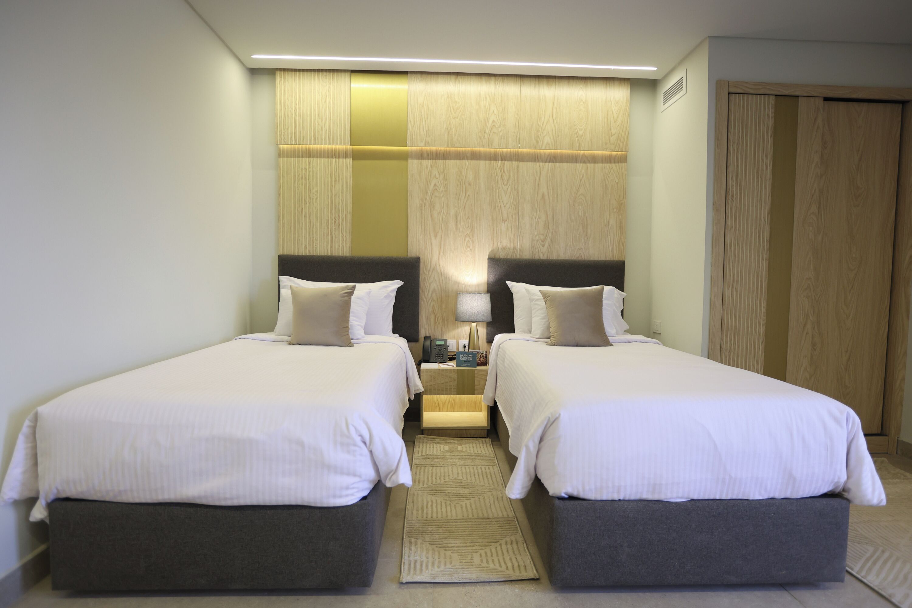 A hotel room with two beds, a nightstand, a lamp, and a wooden panel wall.