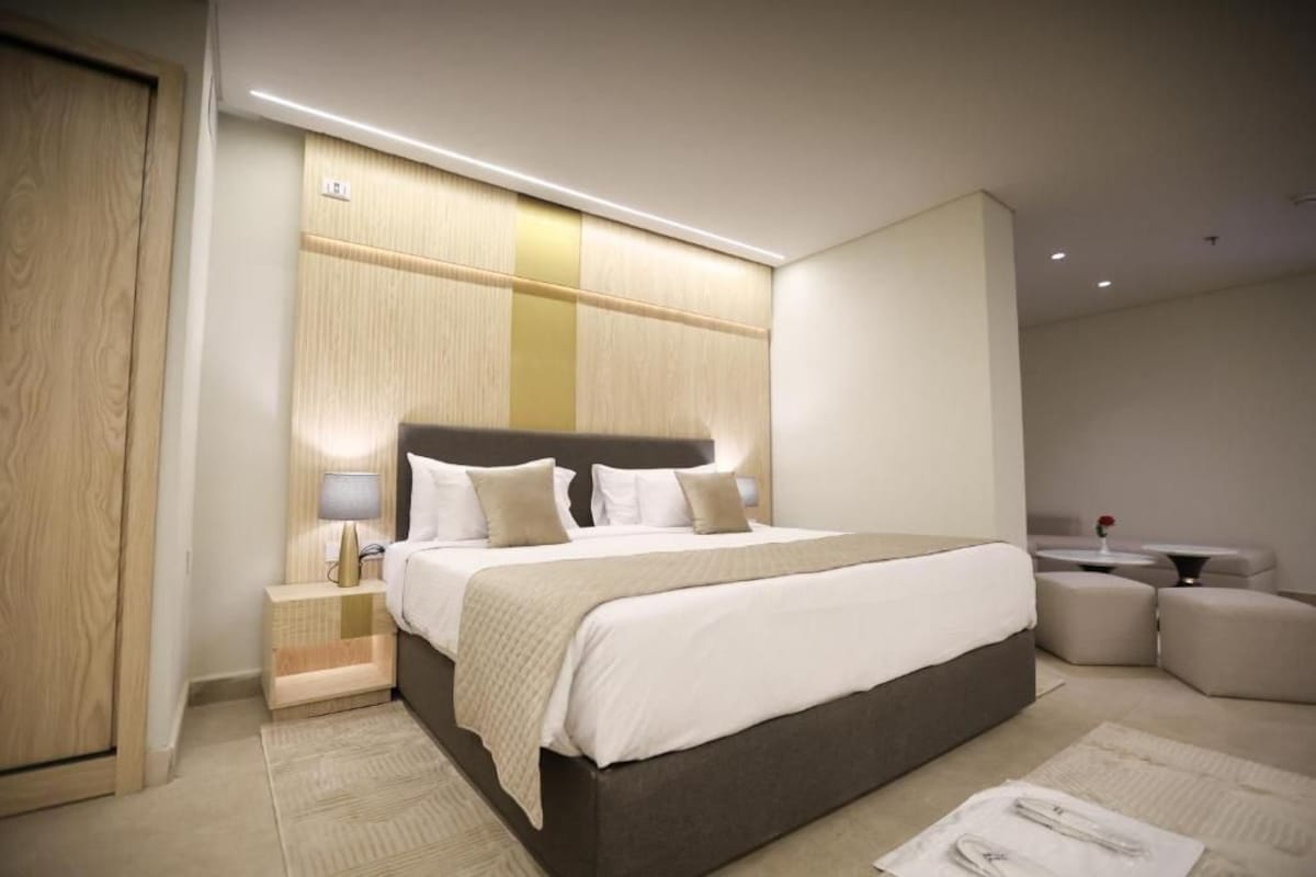 A modern hotel room with a large bed, bedside tables, a small seating area, and a wooden accent wall.