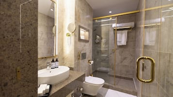 A modern bathroom with a glass-enclosed shower, a sink with toiletries, and a toilet.