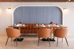A restaurant with a booth seating arrangement, wooden tables, and orange chairs. - Occidental Cairo Grand Museum (Giza)