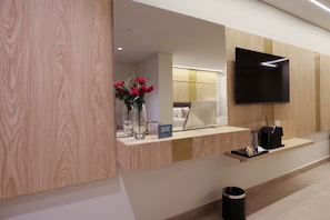 Un mostrador de recepción con un televisor de pantalla plana, un jarrón con flores rojas y un ordenador portátil.
