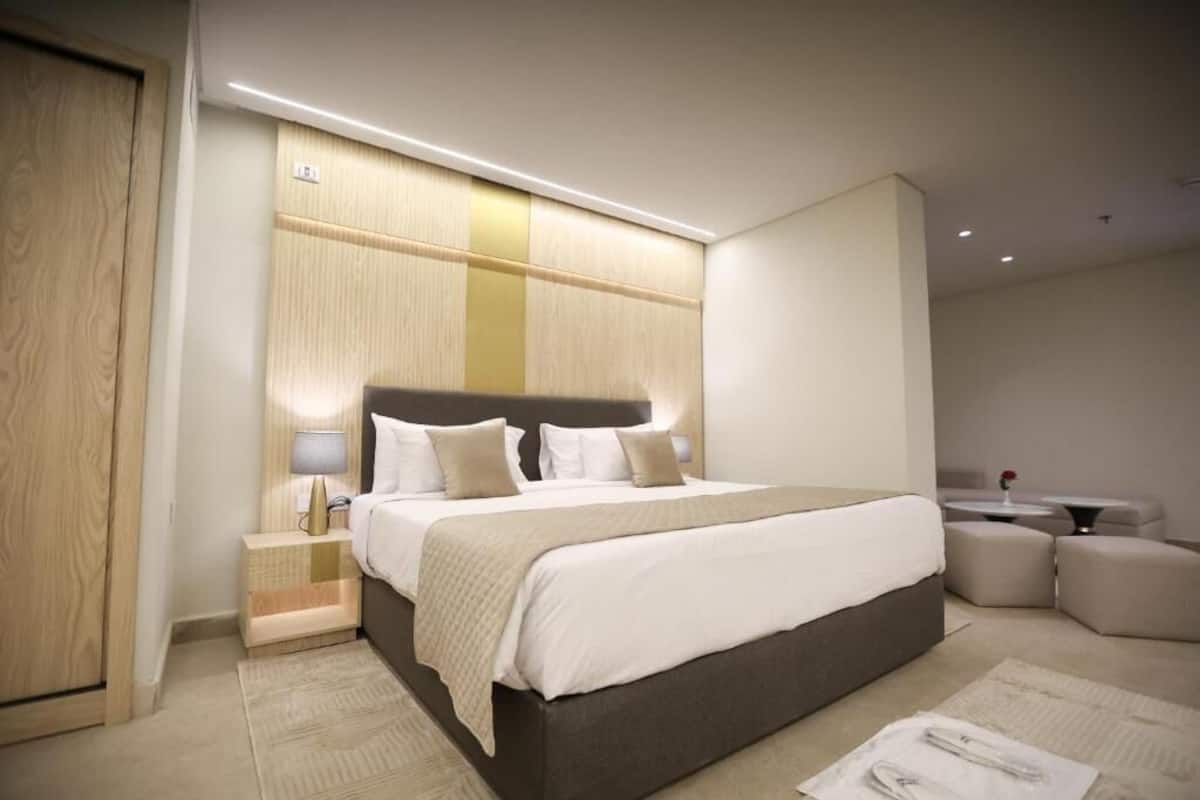 Una habitación de hotel moderna con una cama grande, mesitas de noche, un pequeño rincón de descanso y una pared decorativa de madera.