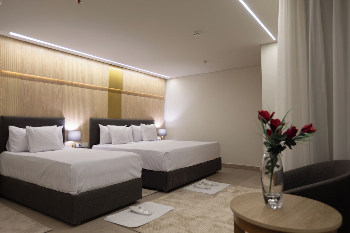 A hotel room with two beds, a small round table with a vase of flowers, and a chair.