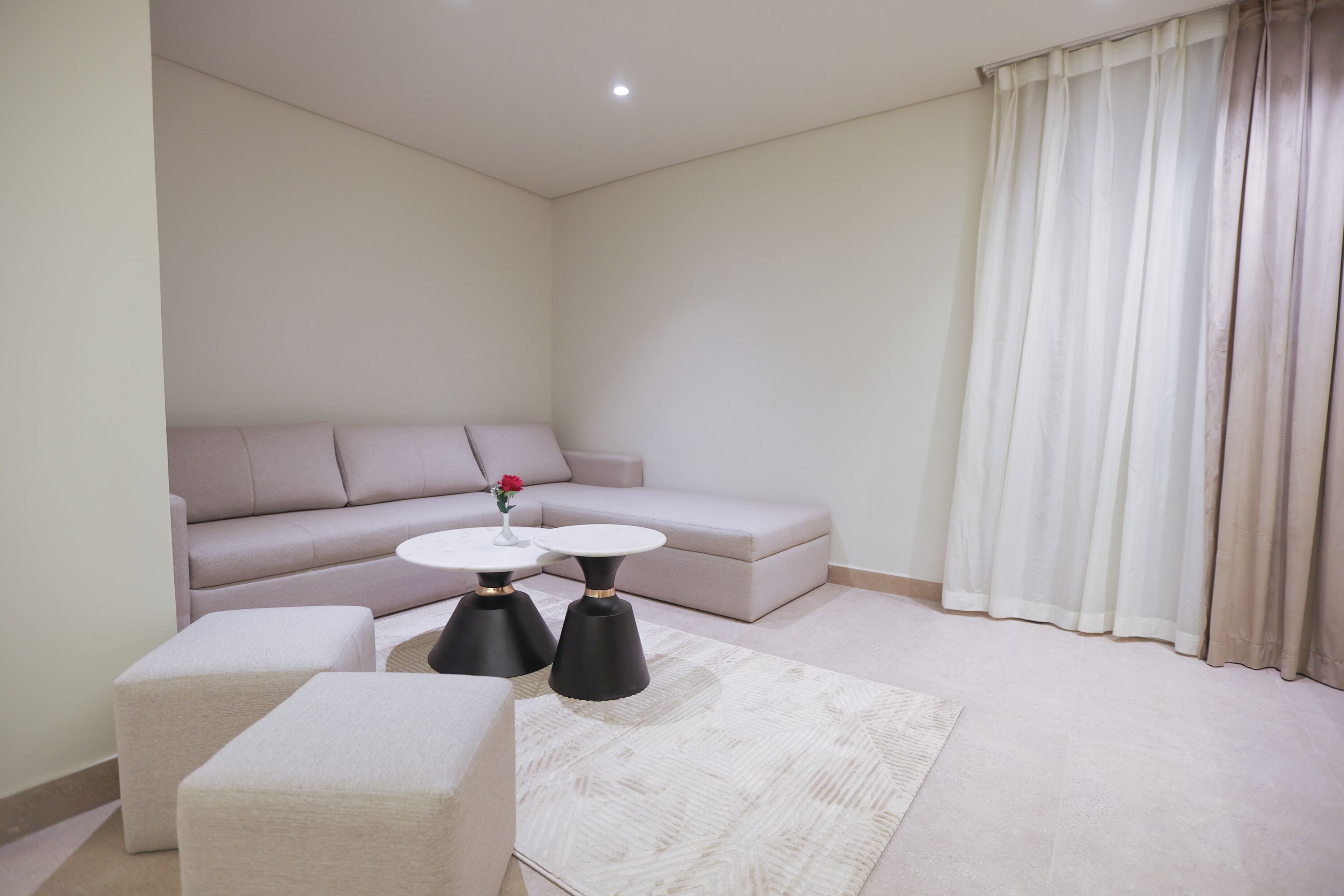 Ein modernes Wohnzimmer mit einer Couch, zwei schwarzen Tischen, einem weißen Teppich und einem Fenster mit Vorhängen.