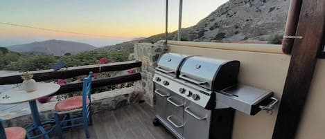Un patio con una parrilla de acero inoxidable, una mesa con sillas y vistas a las montañas.