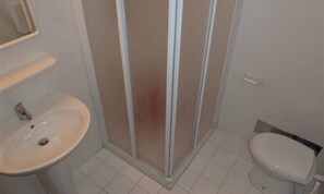 Un baño con lavamanos blanco, inodoro y cabina de ducha con mampara de vidrio.