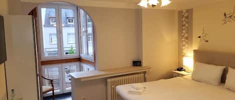 Habitación de hotel con cama, escritorio, silla, radiador, ventana y candelabro.