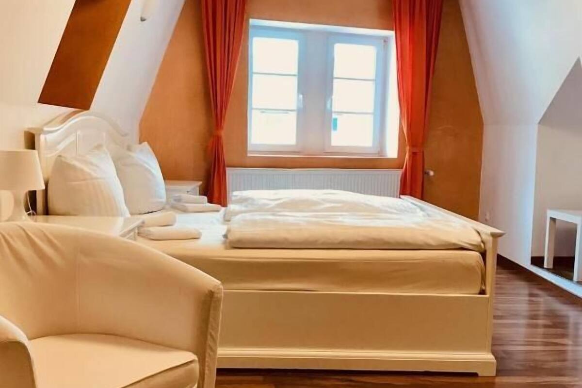 A modern bedroom with a large bed, a chair, and a window with curtains.