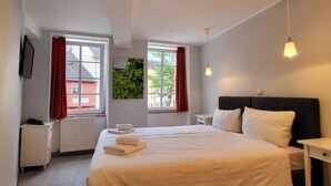 A hotel room with a large bed, two bedside tables, a TV, and windows with red curtains. - Hotel am Markt - Restaurant Meridiana (Saarburg)