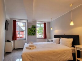 A hotel room with a large bed, two bedside tables, a TV, and windows with red curtains.