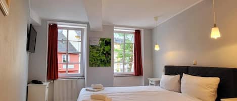 Habitación de hotel con una cama grande, dos mesitas de noche, un televisor en la pared y ventanas con cortinas rojas.