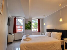 A hotel room with a large bed, two bedside tables, a TV mounted on the wall, and windows with red curtains.