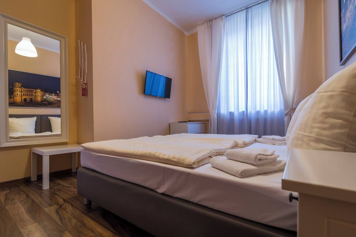 A hotel room with a bed, a bedside table, a TV, a window with curtains, and a wall-mounted picture.