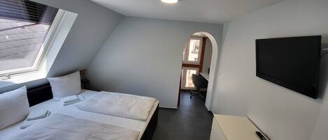 Un dormitorio con una cama, un televisor instalado en la pared y un escritorio con una silla.