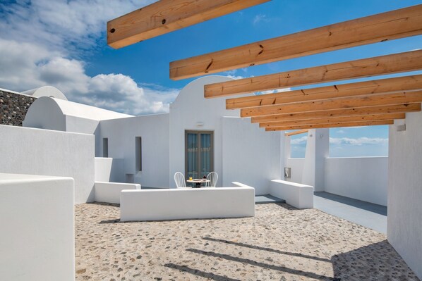 Un patio moderno al aire libre con paredes blancas y piso de piedra, que cuenta con una pérgola de madera y zonas de estar.