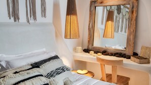 A bedroom with a bed, a wooden chair, a mirror, and a bedside table with candles and decorative items. - Villa - Sleeps 3 - Private Pool-parking (Santorini)