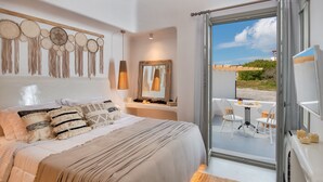 A bedroom with a large bed, a bedside table with a mirror, and a view of the beach through an open door. - Villa - Sleeps 3 - Private Pool-parking (Santorini)