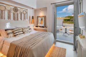 A bedroom with a large bed, a bedside table with a mirror, and a view of the beach through an open door. - Villa - Sleeps 3 - Private Pool-parking (Santorini)