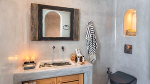 A bathroom with a marble sink, wooden cabinet, and a black toilet. There are candles, toiletries, and a towel rack. - Villa - Sleeps 3 - Private Pool-parking (Santorini)