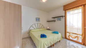 Un dormitorio con una cama, un armario de madera, una mesita con una lámpara y una ventana con cortinas.