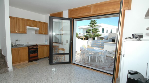 Una cocina con armarios de madera, una estufa y un ventanal corredero que da a un patio exterior con mesa y sillas.