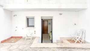 Un edificio blanco con una puerta, una ventana y dos sillas blancas.