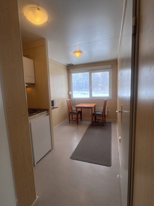 A compact kitchen with a refrigerator, microwave, and stove, a small dining table with two chairs, and a window with a view of a snowy landscape. - Ulseröd Hostel Lysekil (Lysekil)
