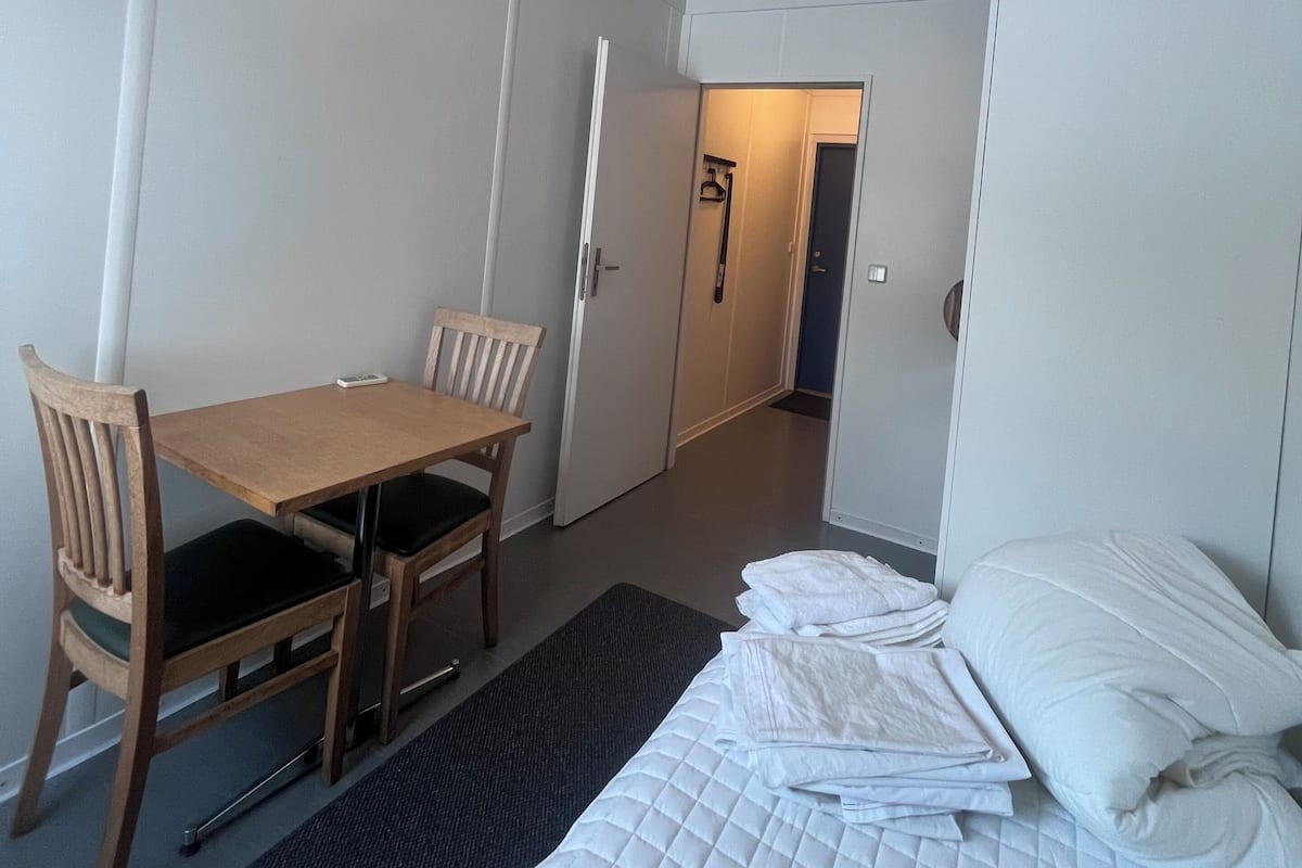 A hotel room with a bed, a desk, two chairs, and a wardrobe.