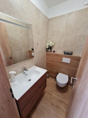 Een kleine badkamer met een witte wastafel, een houten wastafelmeubel en een toilet.