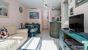 Un espacio habitable pequeño con un sofá, una mesa de comedor con sillas, un televisor y una pequeña cocina.