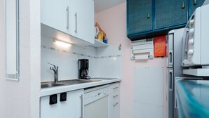 Una cocina compacta con armarios blancos, cafetera, lavabo y refrigerador.