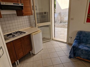 Uma cozinha compacta com fogão a gás, um frigorífico pequeno, armários de madeira e uma porta de vidro deslizante que dá para uma área externa.