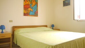 A bedroom with a bed, two bedside lamps, a nightstand, a wall painting, and a window.