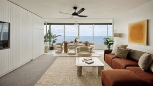 En moderne stue med et stort vindue, en loftsvifte, en sofa, et sofabord og et spiseområde med stole.